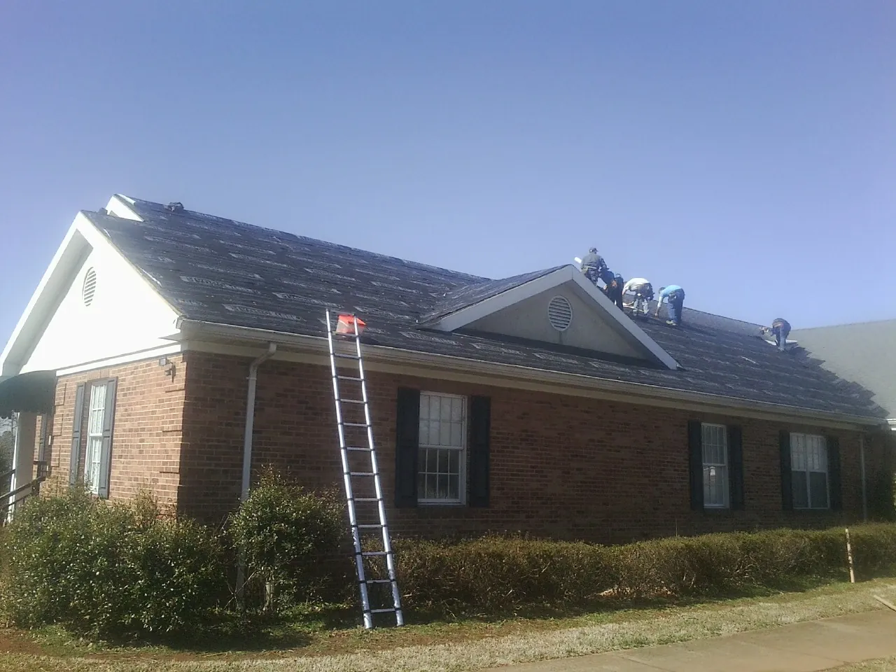 Crew tearing shingles off a brick ranch roof with a ladder set — Emergency Roof Repair work by our crew in Adel
