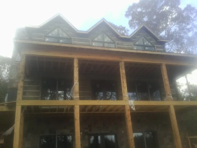 Dormers and porch framing on a large log home under construction — Roof Coating work by our crew in Adel