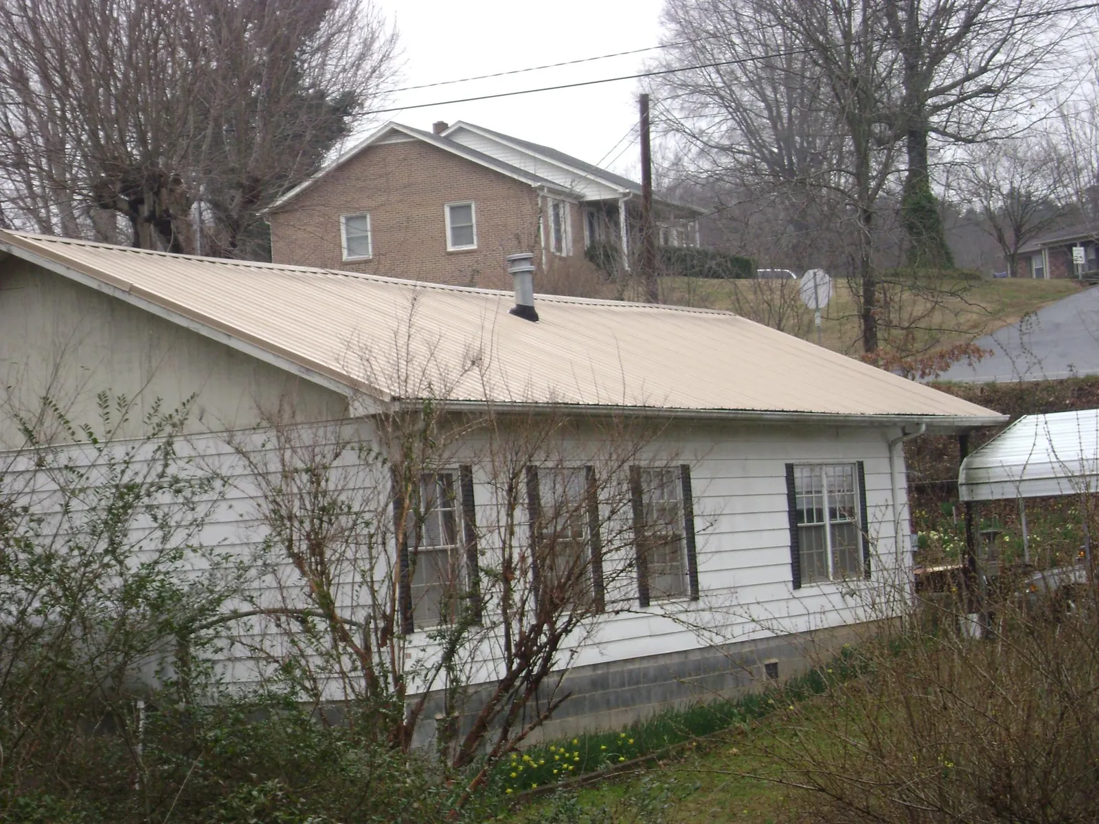 Tan metal roof on a white sided house set into a hillside — Commercial Roofing by Roofing Brothers in Adel